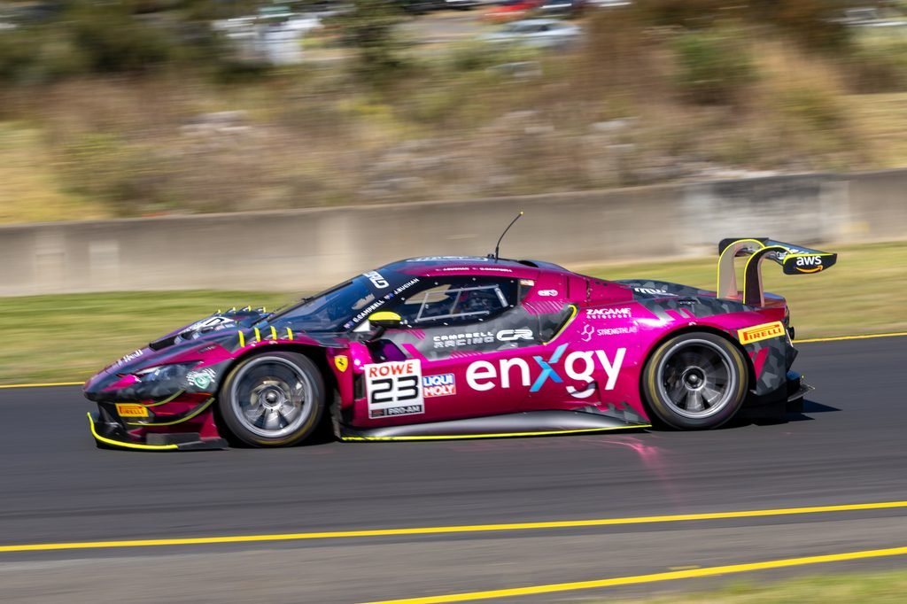0I1A0154 • Sports Rewind Media Pink and black race car with sponsor decals racing at high speed on a track, motion blur suggesting rapid movement.