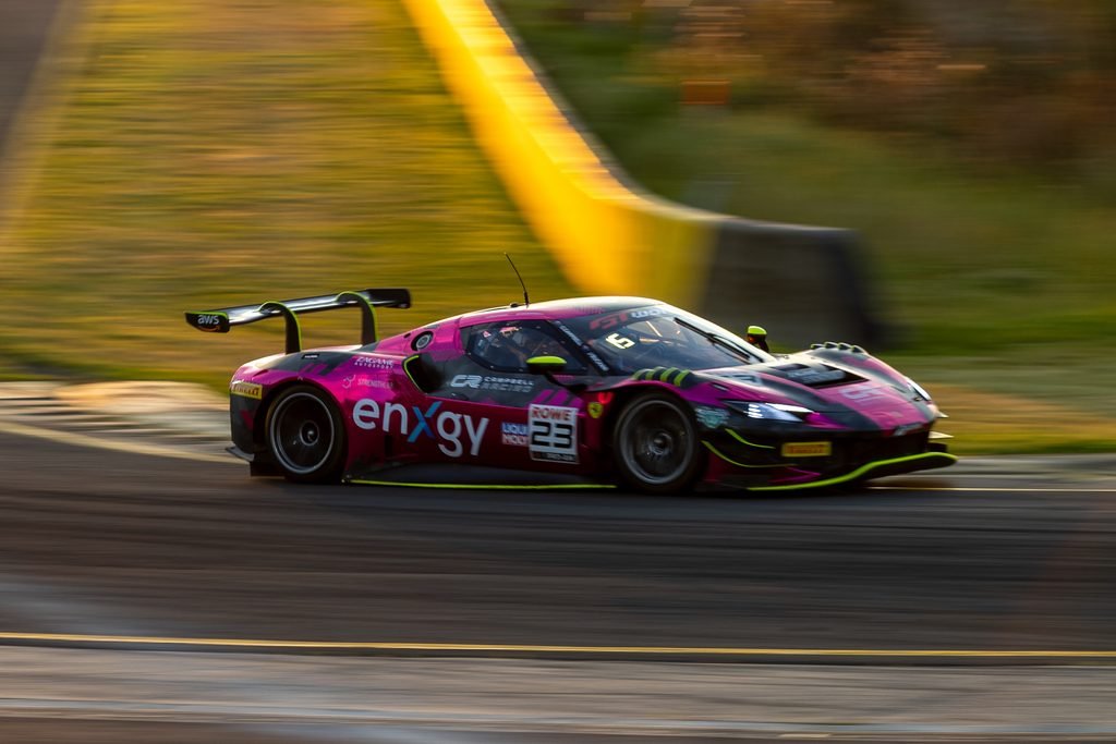0I1A1696 • Sports Rewind Media Pink race car in motion on a race track, sponsor logos visible, blurred background conveying high speed behind the car's winged rear.