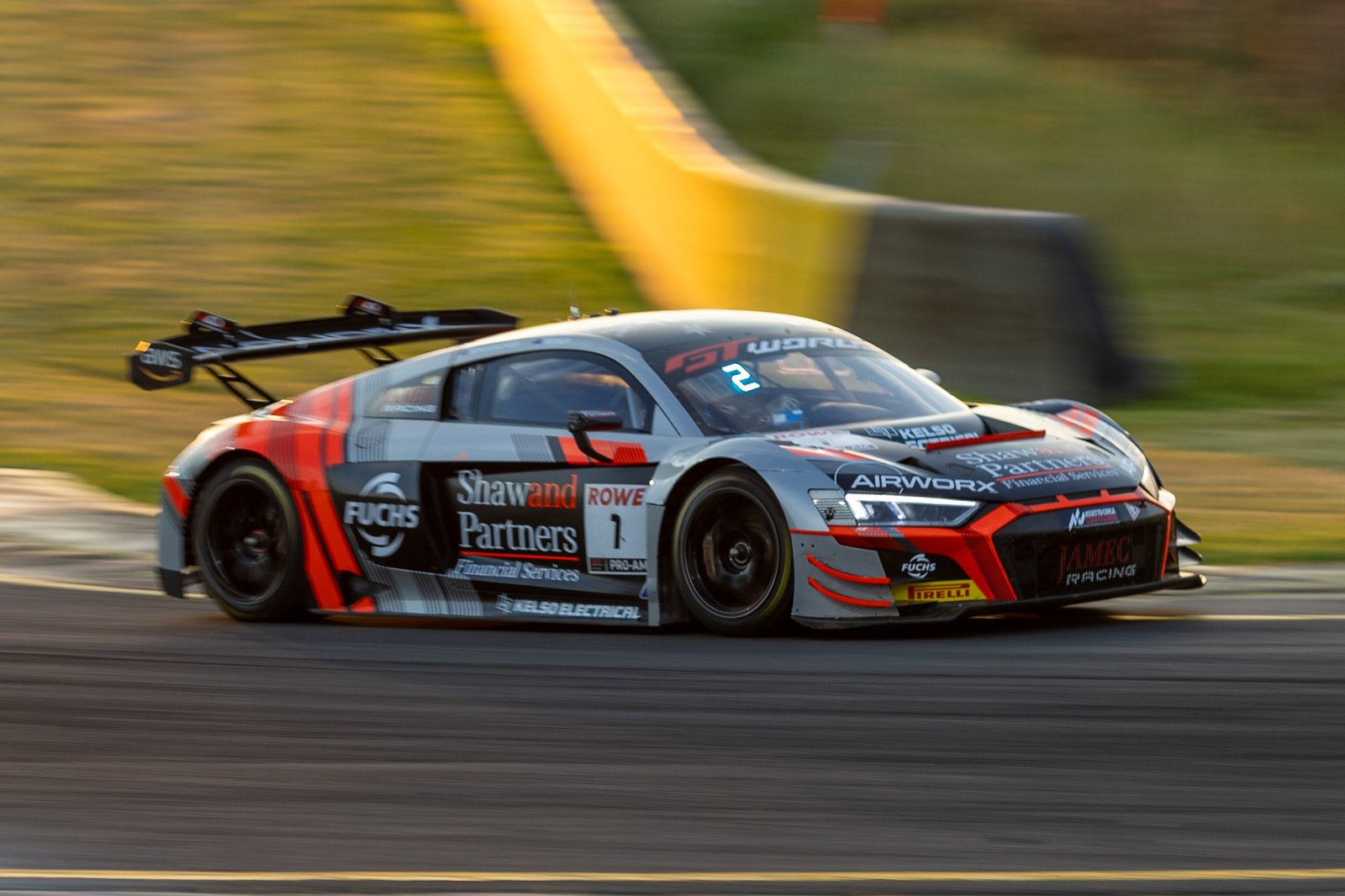 0I1A1697 • Sports Rewind Media Grey and red race car speeding along a track, sponsor logos visible on the side panel and rear wing in motion blur.