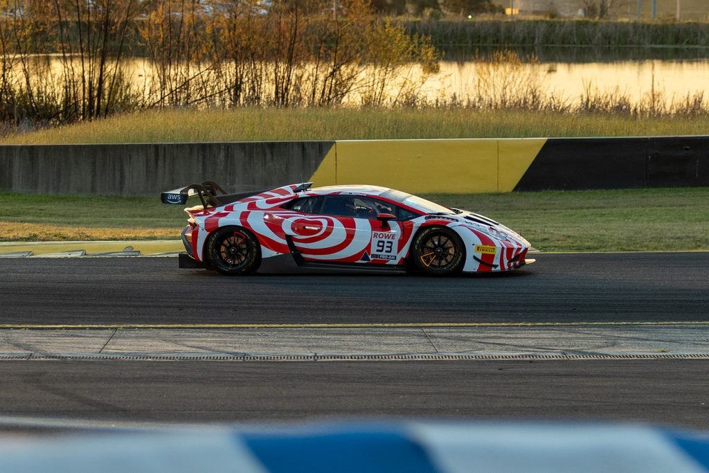 _I1A1648 • Sports Rewind Media Red and white swirl-livery race car (#93) driving on a track beside a yellow/black barrier at sunset.
