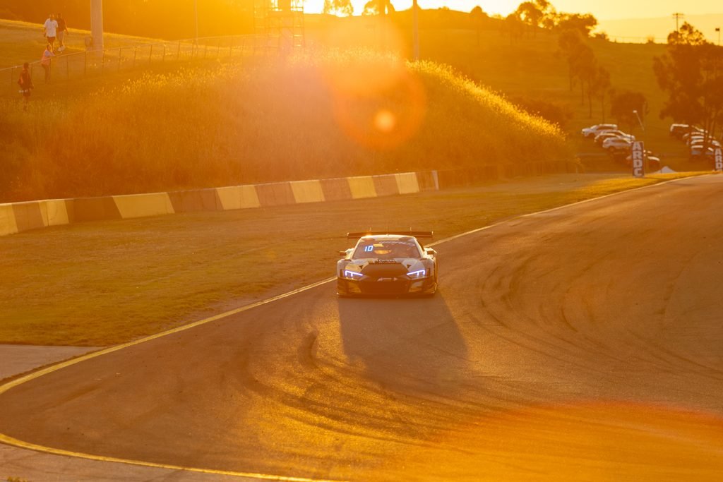 _I1A1667 • Sports Rewind Media Race car speeds along a curved track during golden-hour sunset, headlights on and orange glow reflecting off the road