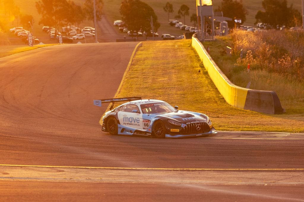 _I1A1678 • Sports Rewind Media Race car on a sunlit track, turning a corner with a grassy embankment and yellow barrier on the right during golden hour sunset