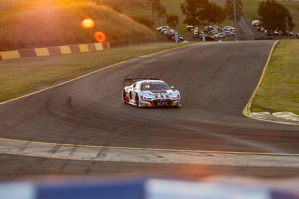 _I1A1732 • Sports Rewind Media Race car on a curving track at sunset, white with KFC branding and a large rear wing, visible tire marks on asphalt.