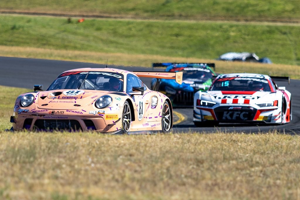 _I1A2402 • Sports Rewind Media Pink race car leading a pack of racing cars on a curved track with grassy infield видно on the sides.