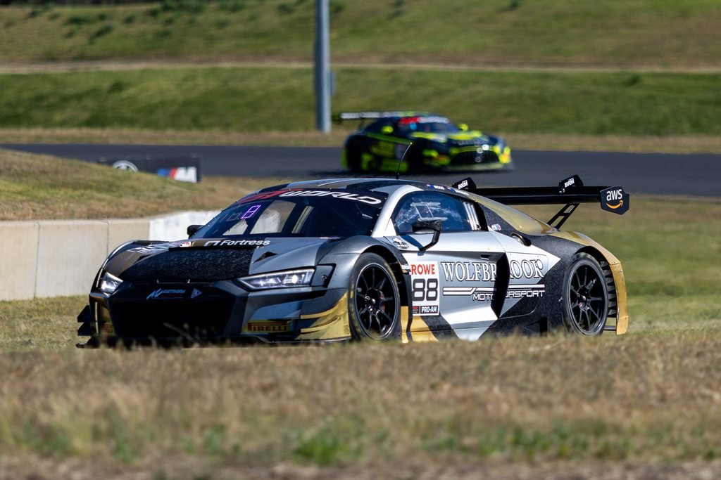 _I1A2409 • Sports Rewind Media Silver and black race car with sponsor decals on a curved track, another neon-yellow/green car blurred in the background.
