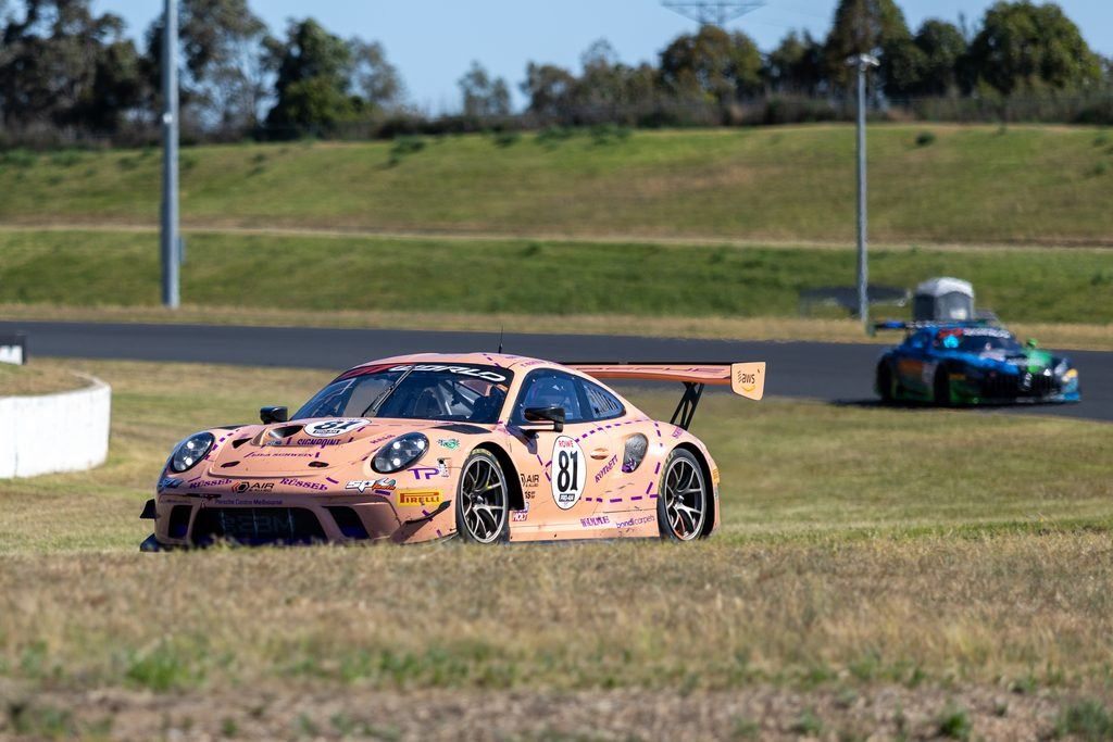 _I1A2422 • Sports Rewind Media Pink race car #81 speeding along a paved track with grass infield and other cars in the background.