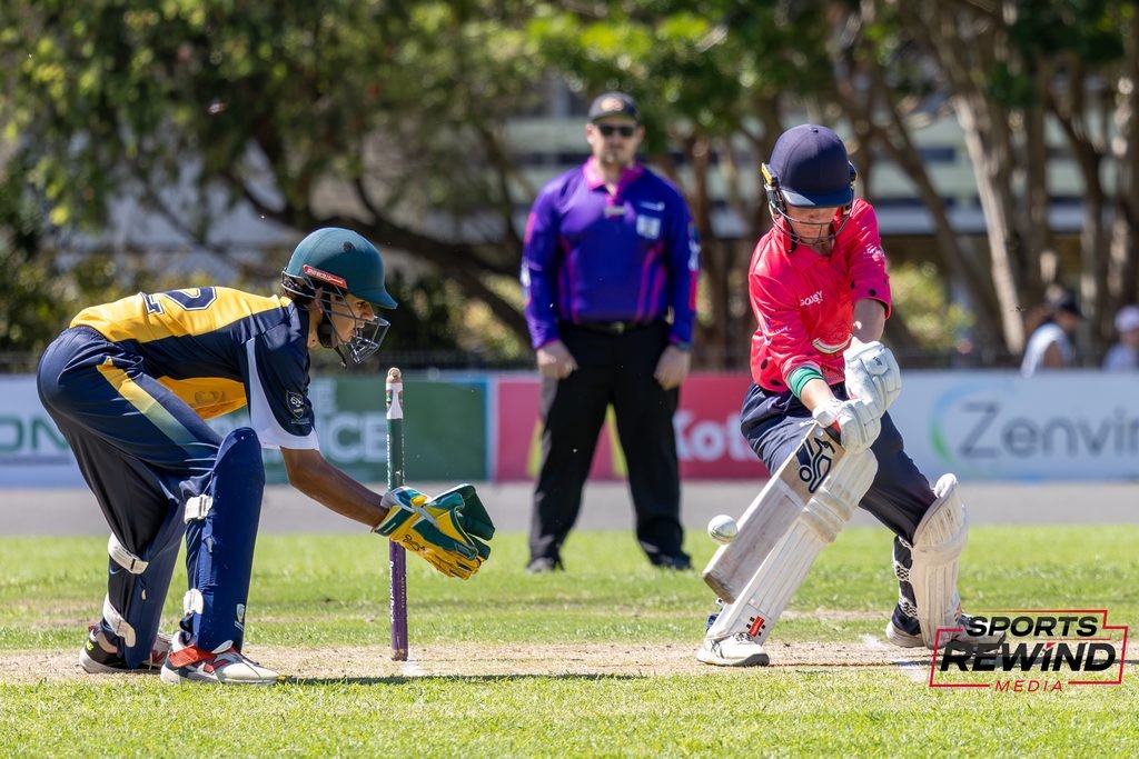 _I1A4790 • Sports Rewind Media Cricket match action: two batsmen at the crease with a wicketkeeper behind them and an umpire in the background on a sunny field.