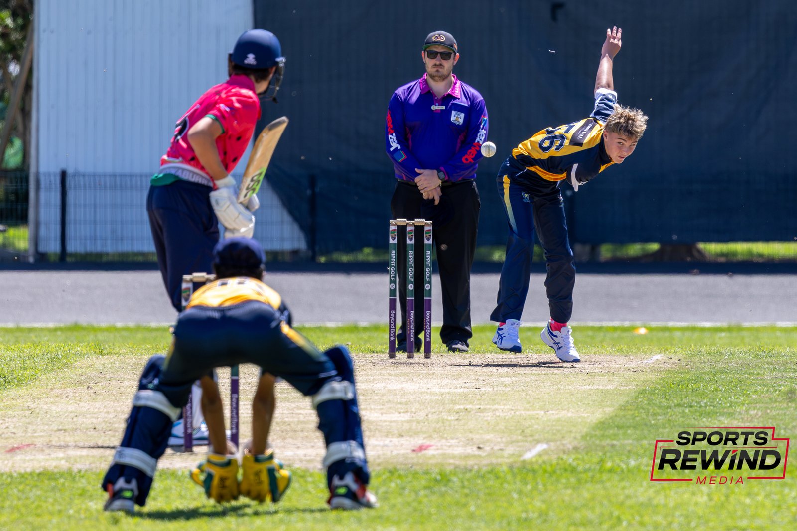 _I1A4894 • Sports Rewind Media Cricket match scene with a bowler delivering toward the batsman near the wickets as the umpire watches.