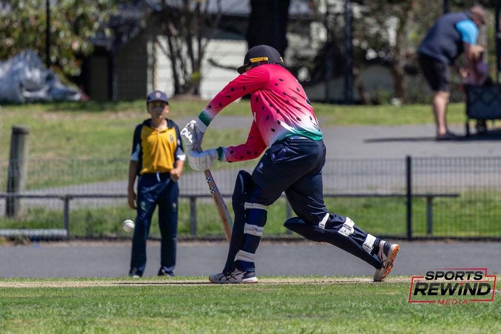 _I1A4938 • Sports Rewind Media Baseball batter in a pink watermelon-pattern jersey runs toward base during a game, with a young fielder watching in the background; sports branding at bottom right.
